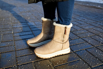 Close view of suede boots on salted pavement during winter road maintenance showing rock salt scattered to prevent slipping and icy sidewalk conditions. Female boots on salted paving slabs