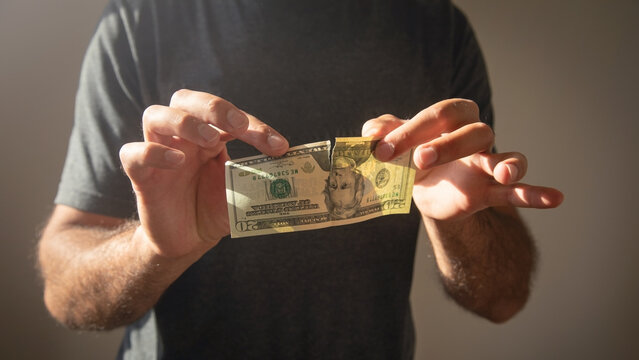 Caucasian man showing torn dollar banknote.