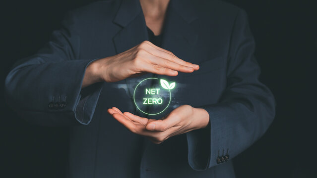 Businesswoman hands surrounding glowing net zero icon with leaf, representing sustainable development, environmental responsibility, and carbon neutrality.