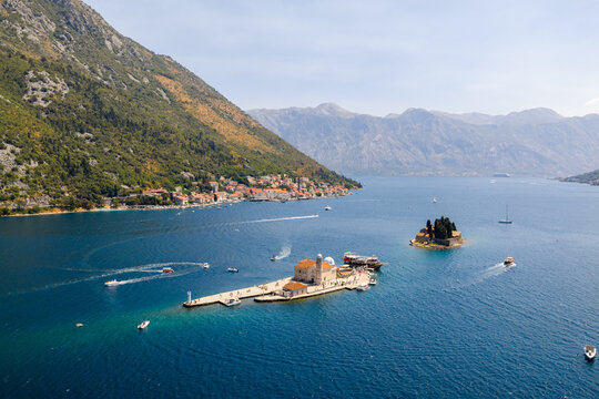 Aerial view of the captivating Our Lady of the Rocks island church and Sveti Dorde island shimmer amidst the azure waters, framed by majestic mountains, Perast, Kotor Municipality, Montenegro.