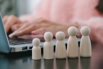 Wooden figures representing diverse individuals in a collaborative workspace setting with a laptop and soft pink tones in the background, ideal for teamwork concepts