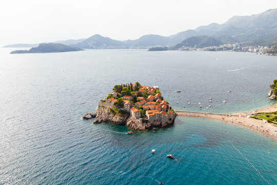 Aerial view of the terracotta rooftops of Sveti Stefan island contrast with the azure sea and the sandy isthmus, Sveti Stefan, Budva Municipality, Montenegro.