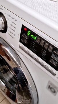 Vertical, close up of a white washing machine control panel. The digital display shows the word 'End' in bright green Cyrillic text, signaling the finished cycle. Chrome and button details are visible
