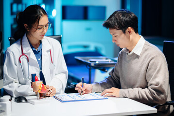 Obraz premium Asian female doctor consulting male patient in clinic. Healthcare, diagnosis, and medical advice concept with real people in hospital office setting.