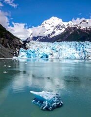 A vibrant, expansive landscape showcases a serene glacial lake, with a bright blue glacier at its edge, framed by mountainous peaks