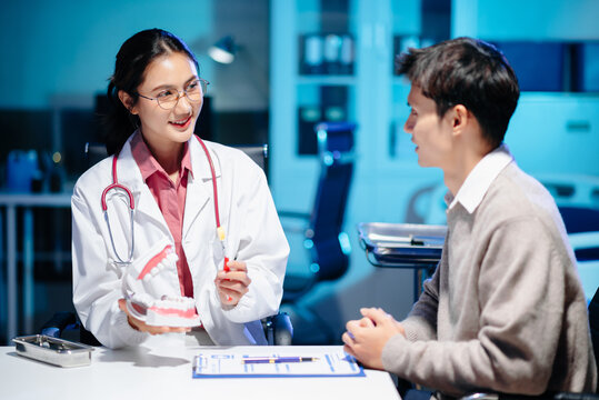 Asian female dentist holding dental model demonstrating brushing technique to young adult asian man patient
