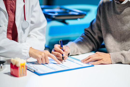 Asian female dentist explains dental model and treatment form to patient during consultation