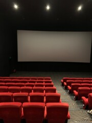 Obraz premium interior of movie theater also known as a cinema. The room features large blank projection screen and rows of red upholstered seats.