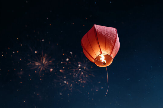 Luminous red sky lantern floating at night with fireworks