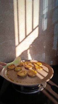 Golden sunlight shining on slices of eggplant being fried in mustard oil on a hot pan in a cozy kitchen, creating a warm and rustic morning cooking atmosphere in natural light
