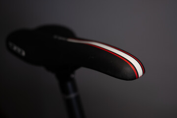 Sleek black road bike saddle with red and white stripes. Selective focus on the modern design against a blurred gray background, perfect for adding text or graphics