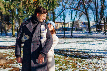 Stylish loving couple hugging walking in winter park. Man and woman wearing warm coats on sunny snowy day