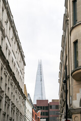 Modern Glass Skyscraper Seen Between Historic Stone Buildings in City Street