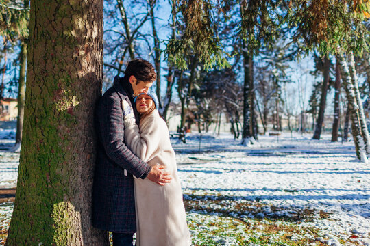 Stylish loving couple hugging walking in winter park. Man and woman wearing warm coats on sunny snowy day - Powered by Adobe