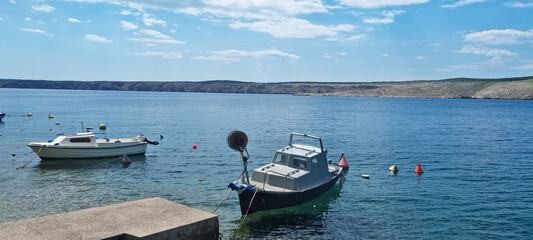 Obraz premium Two small boats are moored in the clear blue Adriatic sea off the coast of Jadranovo, with the rugged, uninhabited shore of Krk Island visible in the distance