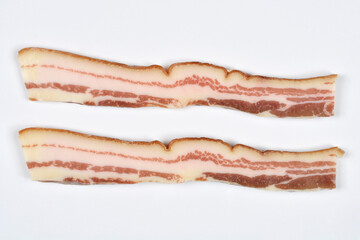 Two long, thin slices of raw streaky bacon with distinct layers of fat and meat are laid horizontally on a white background