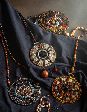 A collection of Dinka beadwork and intricate necklaces are laid out on a dark cloth.