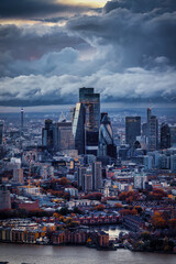 Moody autumn dusk view of the City of London, England, skyline with dark clouds and red coloured trees