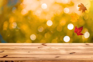 Fotobehang Herfst Wooden surface with falling autumn leaves and blurred golden bokeh background for product presentation  © rehena
