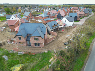 Newly completed large detached family home seen near other private and affordable homes in a British housing development site. Seen near a rural country road.