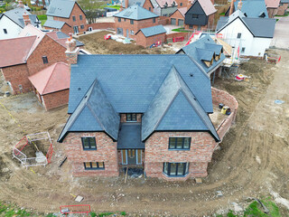 Newly completed large detached family home seen near other private and affordable homes in a British housing development site. Seen with other near completed family homes.