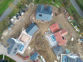 Drone inspection view of a cluster of detached family homes seen near the completed phase on a rural housing development site in Britain. A road intersection is at the top of the image, out of view.
