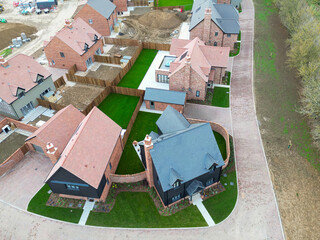 Drone inspection view of newly completed private, detached family homes with new laid lawns on a British rural housing development site. Seen with affordable homes.