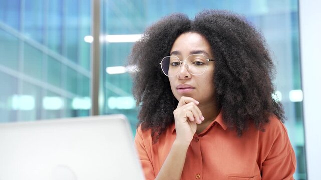 Thoughtful African American businesswoman thinking about problem solving while working on laptop sitting at workplace in business office. Black woman manager is engaged in project or startup. Close up