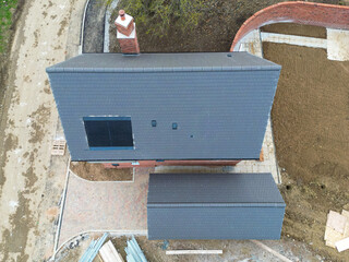 Drone inspection view of a newly completed detached private home showing the new tiled roof and newly fitted, next generation solar panel. A single detached garage is nearby.