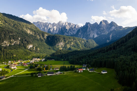 Aerial view of a quaint village nestled in the valley, where emerald meadows meet dense forests and towering, jagged mountains kiss the sky, Gosau, Upper Austria, Austria.