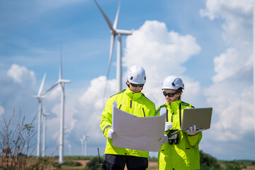 Fototapeta premium Two people are looking at a map of wind turbines. One of them is wearing a yellow jacket. Engineers on wind turbine farm, inspecting and planning for renewable energy project.