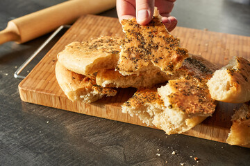 A man holds a loaf of spiced bread on a wooden board. Crispy focaccia.
