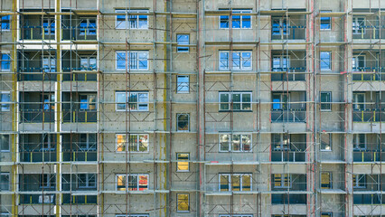 Modern residential building renovation with scaffolding and windows reflecting sunlight, exterior construction maintenance view