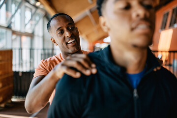 Smiling trainer patting a fit young man on the back after a workout session together at the gym