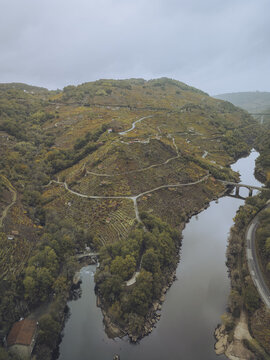Aerial view of the winding river embracing the rugged, vineyard-laden hills of Ribeira Sacra, where earthy tones meet the water's somber reflection, Chantada, Lugo, Spain.
