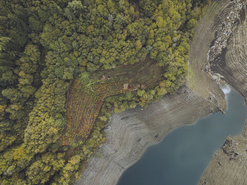 Aerial view of a dramatic contrast between the serene blue river and the rugged, textured shoreline, blending seamlessly into the vibrant autumnal forest, Chantada, Lugo, Spain.