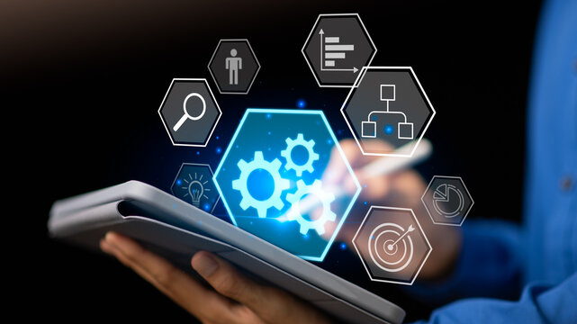 A businessman using a digital tablet with glowing gear and workflow icons, symbolizing process automation, business management, efficiency improvement, and innovation in corporate technology systems.