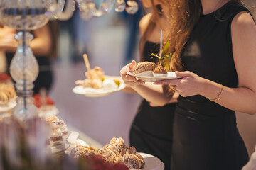 Elegant women enjoying a dessert display at a luxurious event in a well-lit venue during the evening
