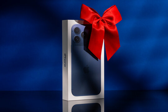 Riga, Latvia - November 11 2025: a box of new Apple iPhone 17 pro max with red bow like a gift on dark blue background. The latest model of Apple mobile phones. Copy space 