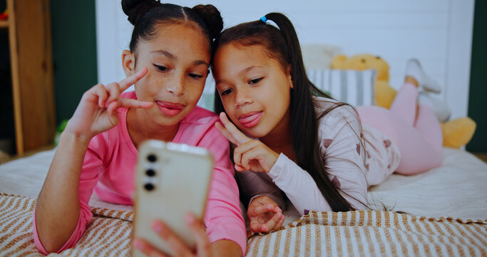 Smile, children and relax with selfie on bed for photography, social media post and bonding together. Happy, girls and profile picture for family blog, siblings memory and weekend in home bedroom - Powered by Adobe