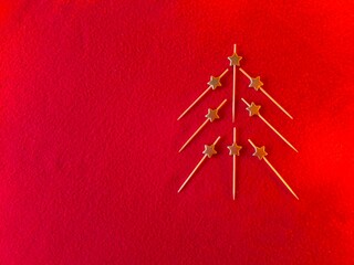creative Christmas tree made of toothpicks on a red background with gold stars