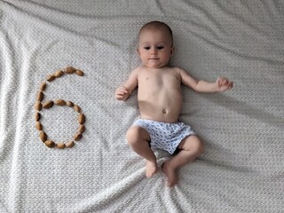 A six-month-old baby celebrates his monthly milestone, lying next to the number six formed by walnuts.

