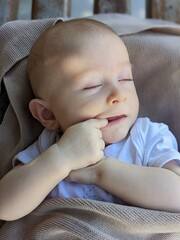 A three-month-old baby sleeps peacefully with his finger in his mouth due to early teething discomfort.

