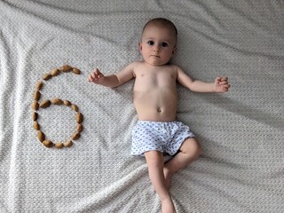 A six-month-old baby lies on a blanket, surrounded by a number six made of walnuts for his monthly milestone.

