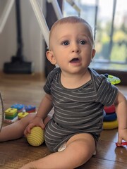 A seven-month-old baby sitting on the floor surrounded by his colorful educational toys.

