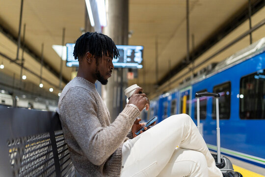 Young black man waiting for subway train using phone - Powered by Adobe
