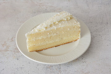 Delicious Slice of Coconut Cake with coconut chips on a White saucer