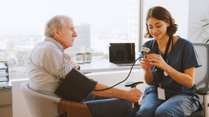 Nurse Wearing Scrubs In Hospital Office Checking Senior Male Patients Blood Pressure
