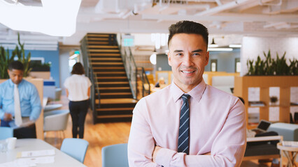 Portrait Of Businessman In Modern Office With Colleagues Meeting Around Table In Background