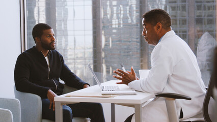 Man Having Consultation With Male Doctor In Hospital Office